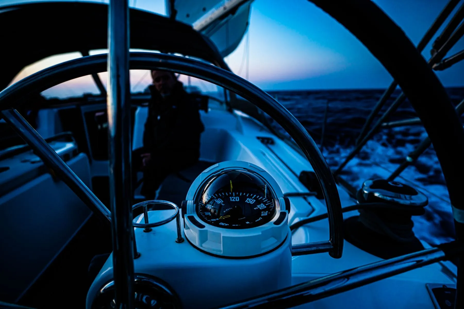 A sailboat’s wheel and binnacle compass lit at twilight