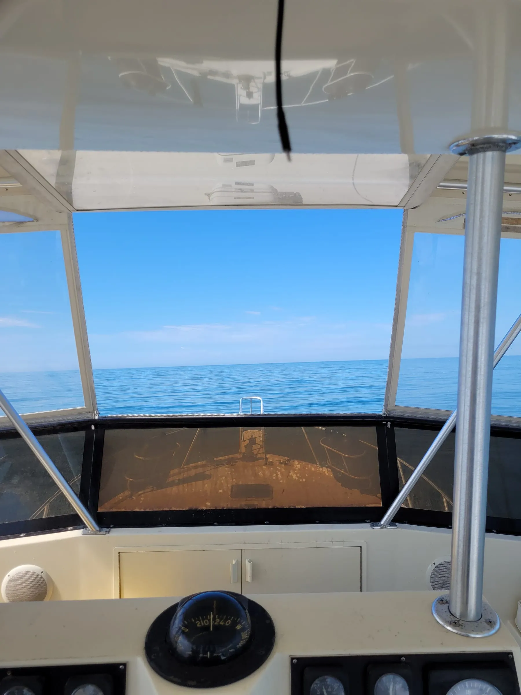 The view forward from a flybridge helm offshore, compass in the foreground and open water ahead
