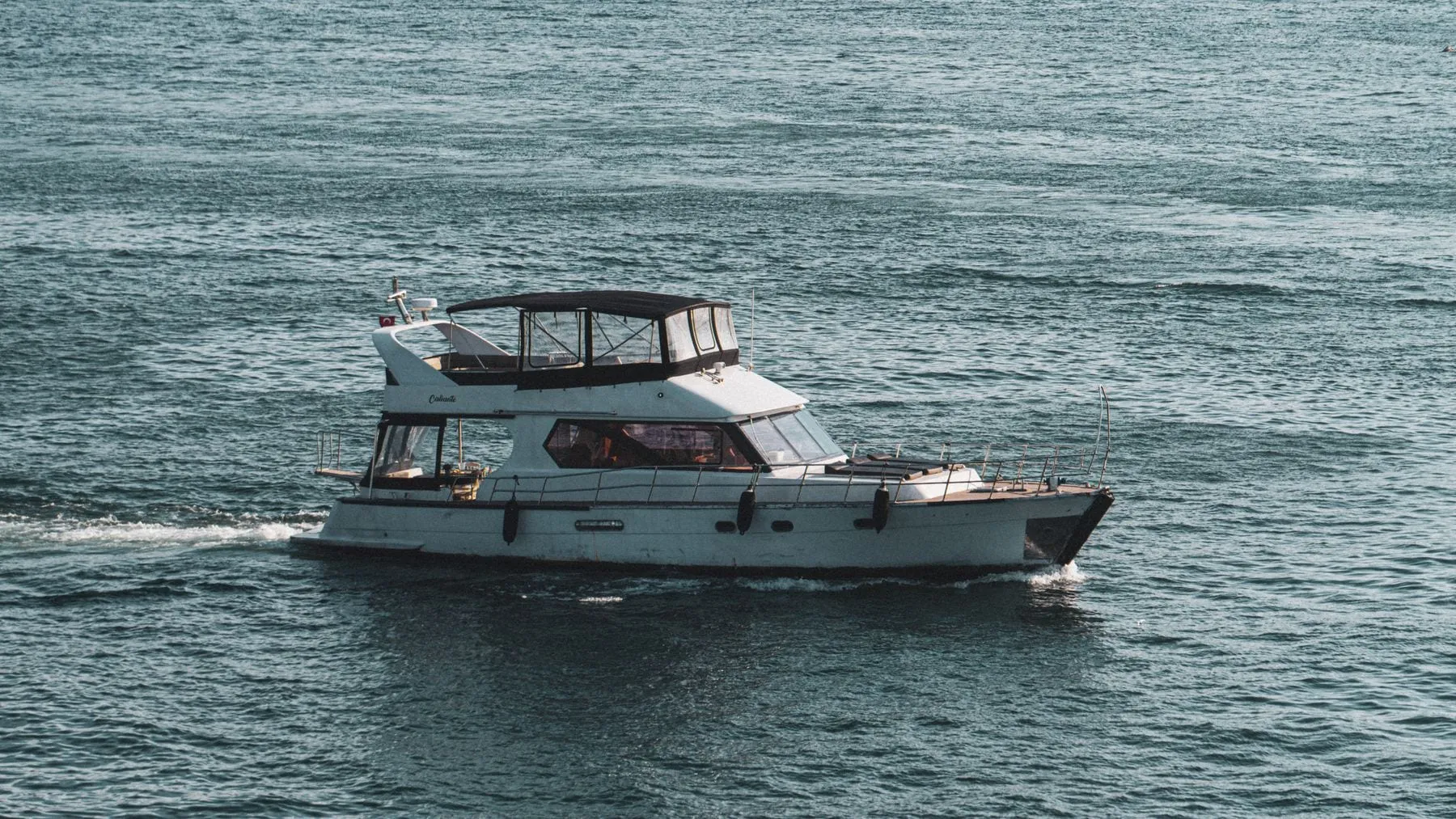 A flybridge motor yacht underway on open water, throwing a wake