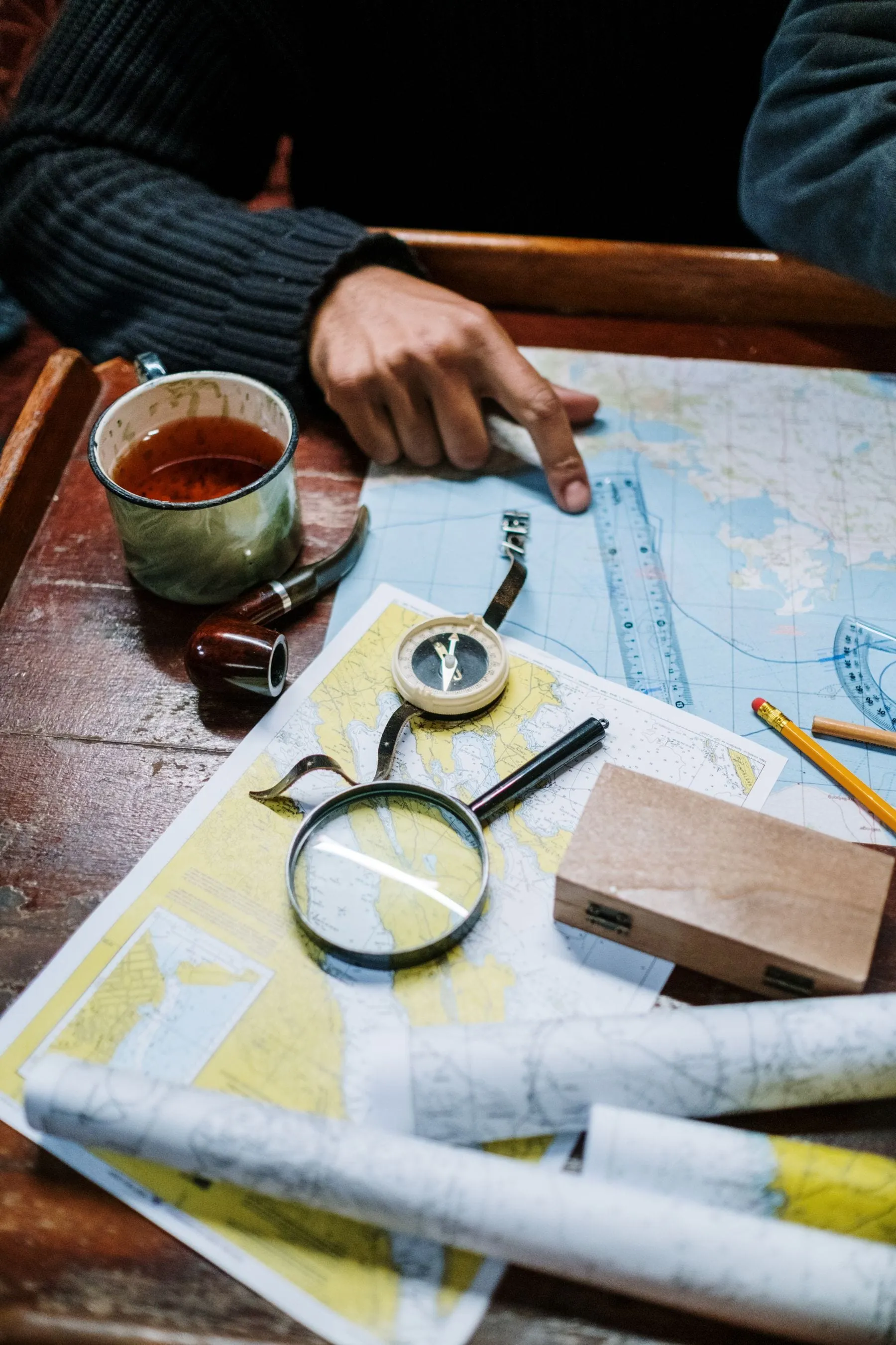 A chart on a wooden table with dividers, a magnifier, a pencil and a mug of coffee