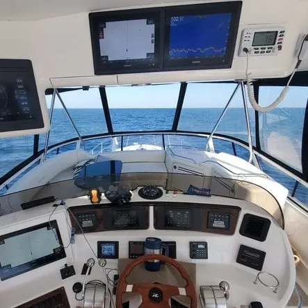 An enclosed flybridge helm with twin chartplotter screens, wheel and throttle levers, open water ahead