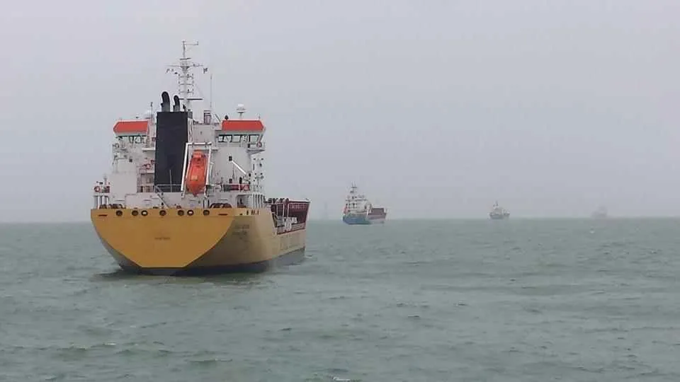 Commercial ships at anchor in grey haze, with more vessels on the horizon