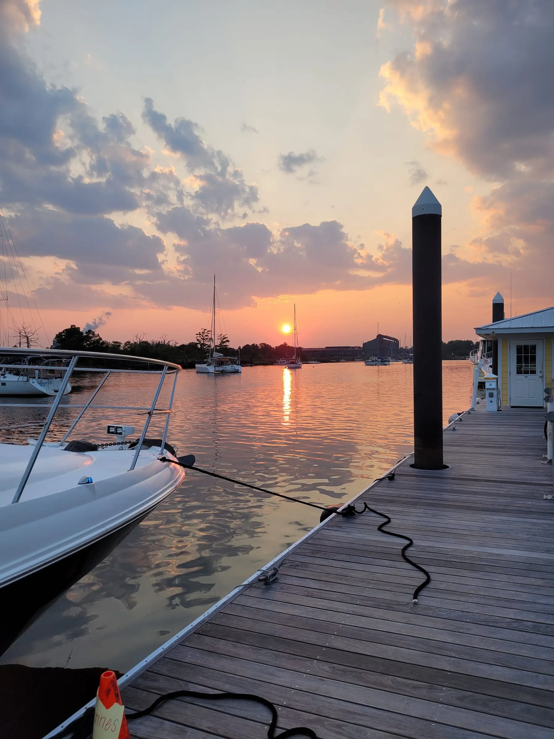 Sunset over a marina seen from a boat’s deck, with a piling and dock in view